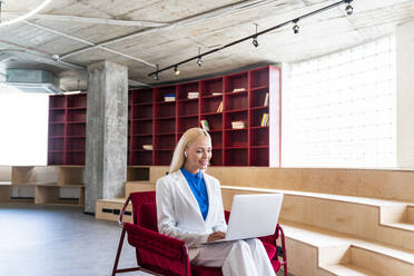 Blonde Geschäftsfrau mit In-Ear-Kopfhörern bei der Arbeit am Laptop im Büro - OIPF01303