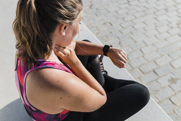 Female athlete looking at smart watch while checking pulse on neck during sunny day - JRVF01858