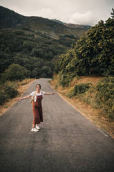 Happy woman with arms outstretched enjoying while standing on road - GRCF00911