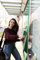 Lächelnde Frau kauft Fahrkarte an der Straßenbahnhaltestelle - VABF04323