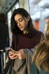 Woman using smart phone while travelling in tram - VABF04326