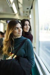 Freundinnen, die während der Fahrt in der Straßenbahn durch das Fenster schauen - VABF04327