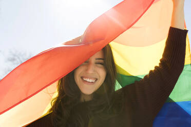 Glückliche Frau mit Regenbogenfahne an einem sonnigen Tag - VABF04342