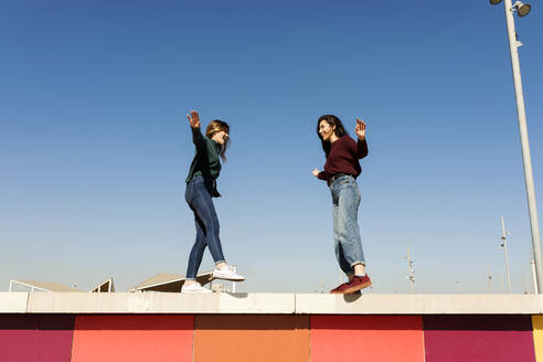 Verspielte Freundinnen, die auf einer Stützmauer stehen und balancieren - VABF04349