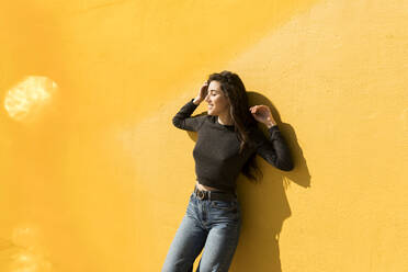 Young woman leaning on yellow wall - VABF04366