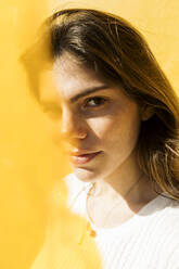 Junge Frau mit braunen Haaren vor einer gelben Wand an einem sonnigen Tag - VABF04371
