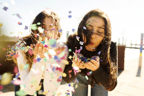 Young women blowing confetti during sunny day - VABF04377