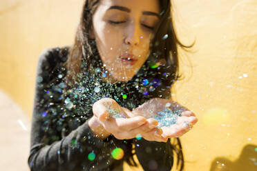 Young woman blowing multi-colored glitter - VABF04379