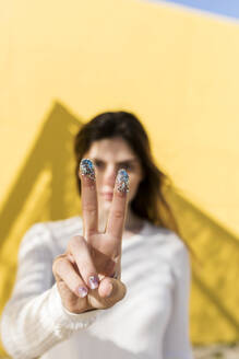 Frau gestikuliert Friedenszeichen mit Glitzer an den Fingern - VABF04382