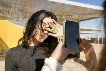 Frau fotografiert Freundin mit Glitzer auf der Handfläche an einem sonnigen Tag - VABF04385