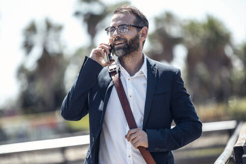 Männlicher Berufstätiger, der an einem sonnigen Tag mit einem Mobiltelefon spricht - JSRF01633