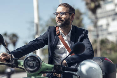 Businessman with helmet and crossbody bag sitting on motor scooter - JSRF01639