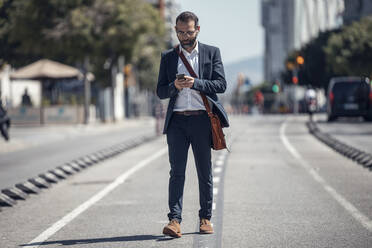 Male business professional using mobile phone while walking in city - JSRF01648