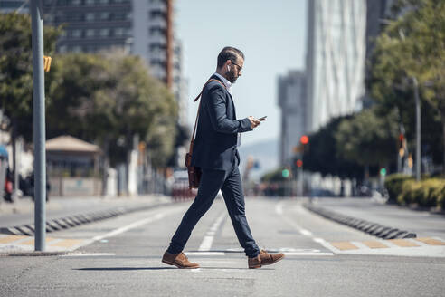 Männlicher Berufstätiger, der beim Spazierengehen in der Stadt ein Mobiltelefon benutzt - JSRF01651