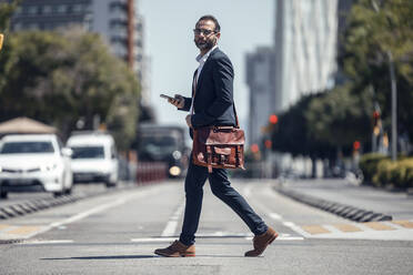 Male business professional with crossbody bag and mobile phone on street - JSRF01652