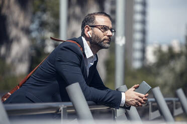 Thoughtful businessman with mobile phone leaning on railing - JSRF01653