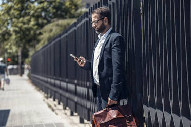 Male business professional using mobile phone on footpath - JSRF01657