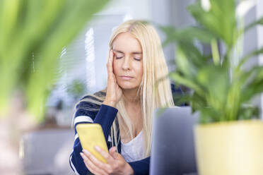 Müde weibliche Berufstätige mit Smartphone im Heimbüro - WPEF05297
