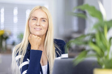 Smiling blond female freelancer with hand on chin at home office - WPEF05303