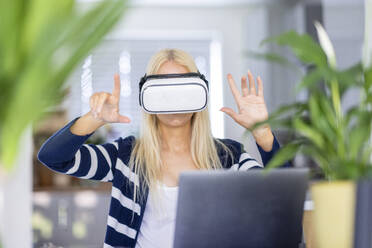 Reife Geschäftsfrau gestikuliert, während sie ein Virtual-Reality-Headset im Heimbüro trägt - WPEF05305