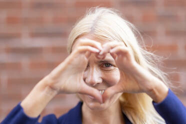 Mature woman making heart symbol with hands - WPEF05306
