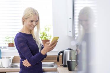 Reife Frau benutzt Mobiltelefon in der Küche - WPEF05313