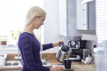 Frau gießt heißes Wasser in Tasse bei der Zubereitung von Kaffee in der Küche zu Hause - WPEF05314