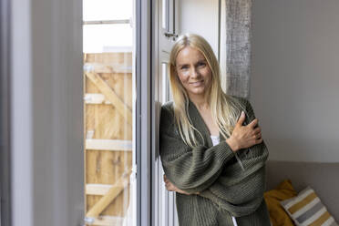 Mature woman in sweater leaning on glass door - WPEF05315