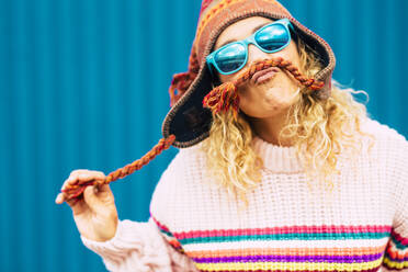 Verspielte Frau mit Sonnenbrille macht Schnurrbart aus Strickmütze - SIPF02405