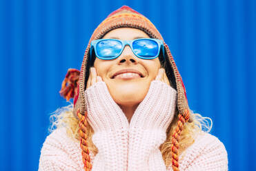 Lächelnde Frau mit Sonnenbrille und Strickmütze, die ihr Gesicht berührt - SIPF02406