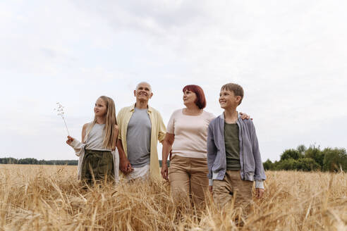 Geschwister gehen mit Großeltern auf einem Weizenfeld spazieren - EYAF01744
