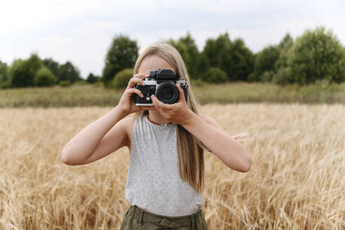 Blond girl photographing through camera on wheat field - EYAF01745