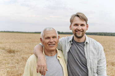 Lächelnder Sohn mit Arm um den älteren Vater auf dem Feld - EYAF01751