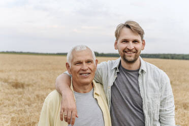 Smiling son with arm around senior father on field - EYAF01751