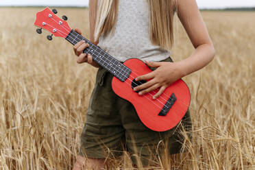 Auf einem Weizenfeld stehendes, Gitarre spielendes Mädchen - EYAF01756