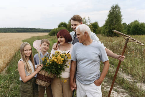 Mehrgenerationenfamilie mit Rainfarnblumen und Gartengeräten auf einem landwirtschaftlichen Feld - EYAF01757
