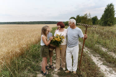 Großeltern und Kinder mit Rainfarnblüten auf einem Feld - EYAF01760