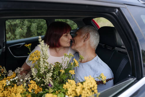 Romantisches älteres Paar mit Tansy-Blumen sitzend und sich küssend im Auto - EYAF01768