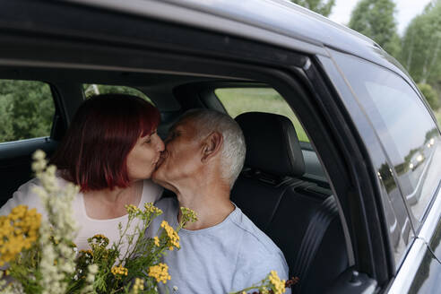 Zärtliches Paar, das sich küsst, während es mit einem Blumenstrauß im Auto sitzt - EYAF01769