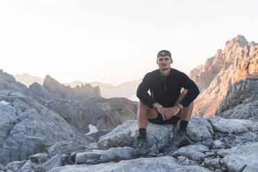 Junger männlicher Tourist auf einem Felsen sitzend, Picos de Europe, Kantabrien, Spanien - JAQF00769