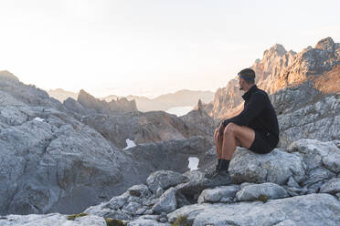 Male tourist looking at Picos de Europe mountain ranges at sunrise, Cantabria, Spain - JAQF00770