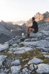 Junger Mann sitzt auf einem Felsen in der Bergkette Picos de Europe, Kantabrien, Spanien - JAQF00771
