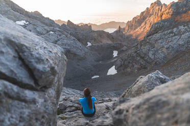 Junge Touristin, die auf einem Felsen sitzend die Bergkette betrachtet, Picos de Europe, Kantabrien, Spanien - JAQF00772