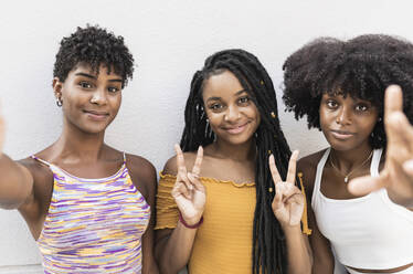 Junge Frauen gestikulieren vor einer Mauer ein Friedenszeichen - JCCMF03908