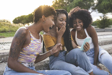 Surprised female friends looking at mobile phone in park - JCCMF03912