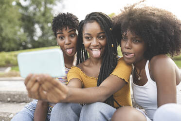 Junge Frauen strecken ihre Zunge heraus, während sie ein Selfie mit ihrem Handy im Park machen - JCCMF03913