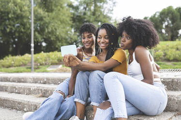 Happy female friends taking selfie on smart phone in park - JCCMF03914