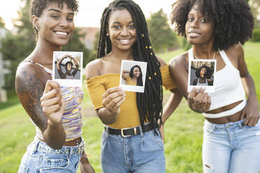 Lächelnde junge Frauen zeigen Fotos im Park - JCCMF03927