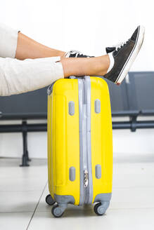 Frau, die im Abflugbereich eines Flughafens die Beine auf das Gepäck legt - JAQF00781