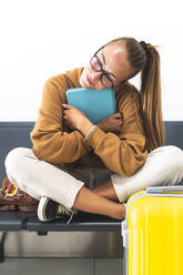 Woman holding digital tablet while sitting cross-legged on bench - JAQF00783